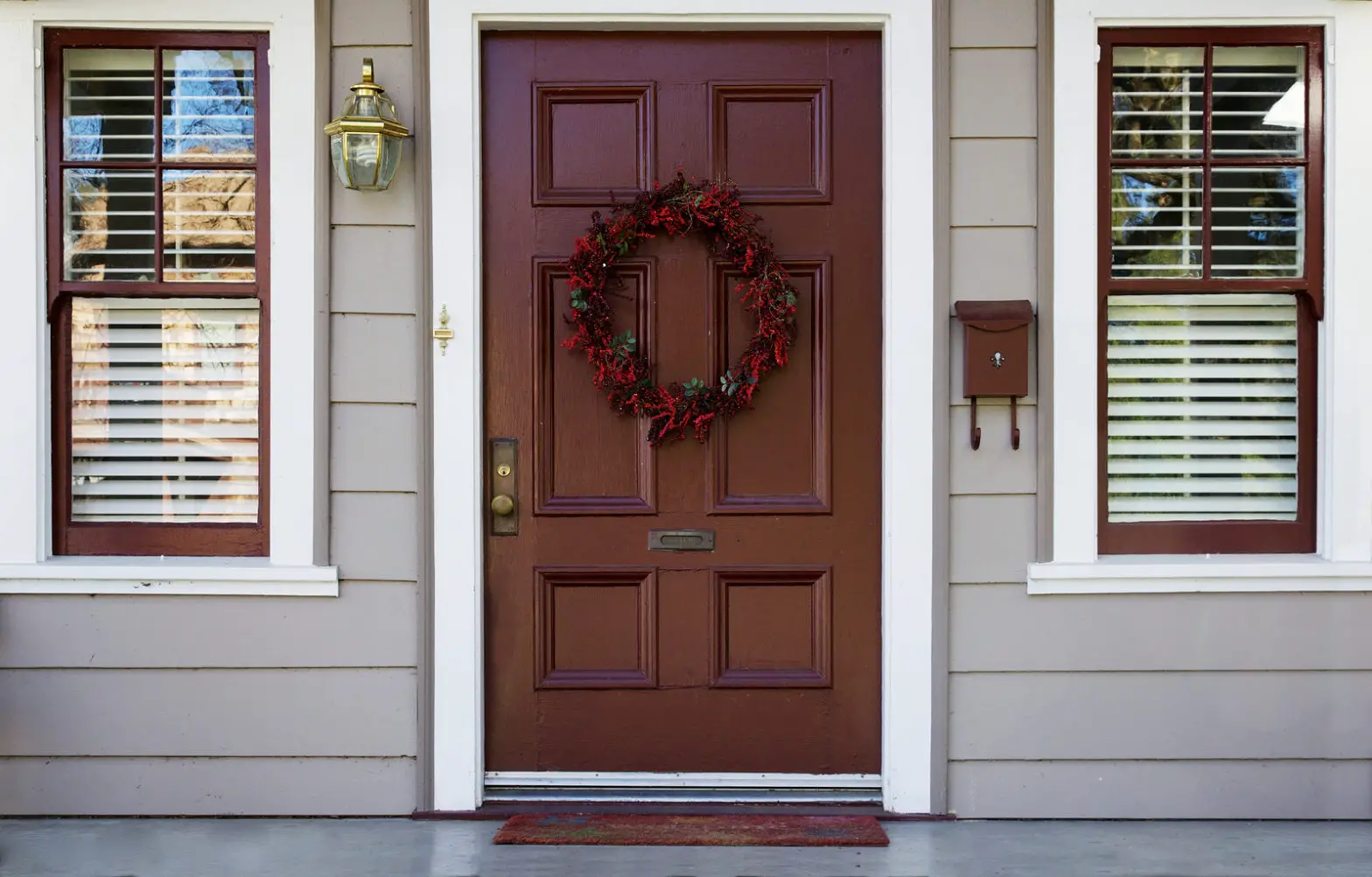 Home burgundy door with wreath with two white trimed blinded windows