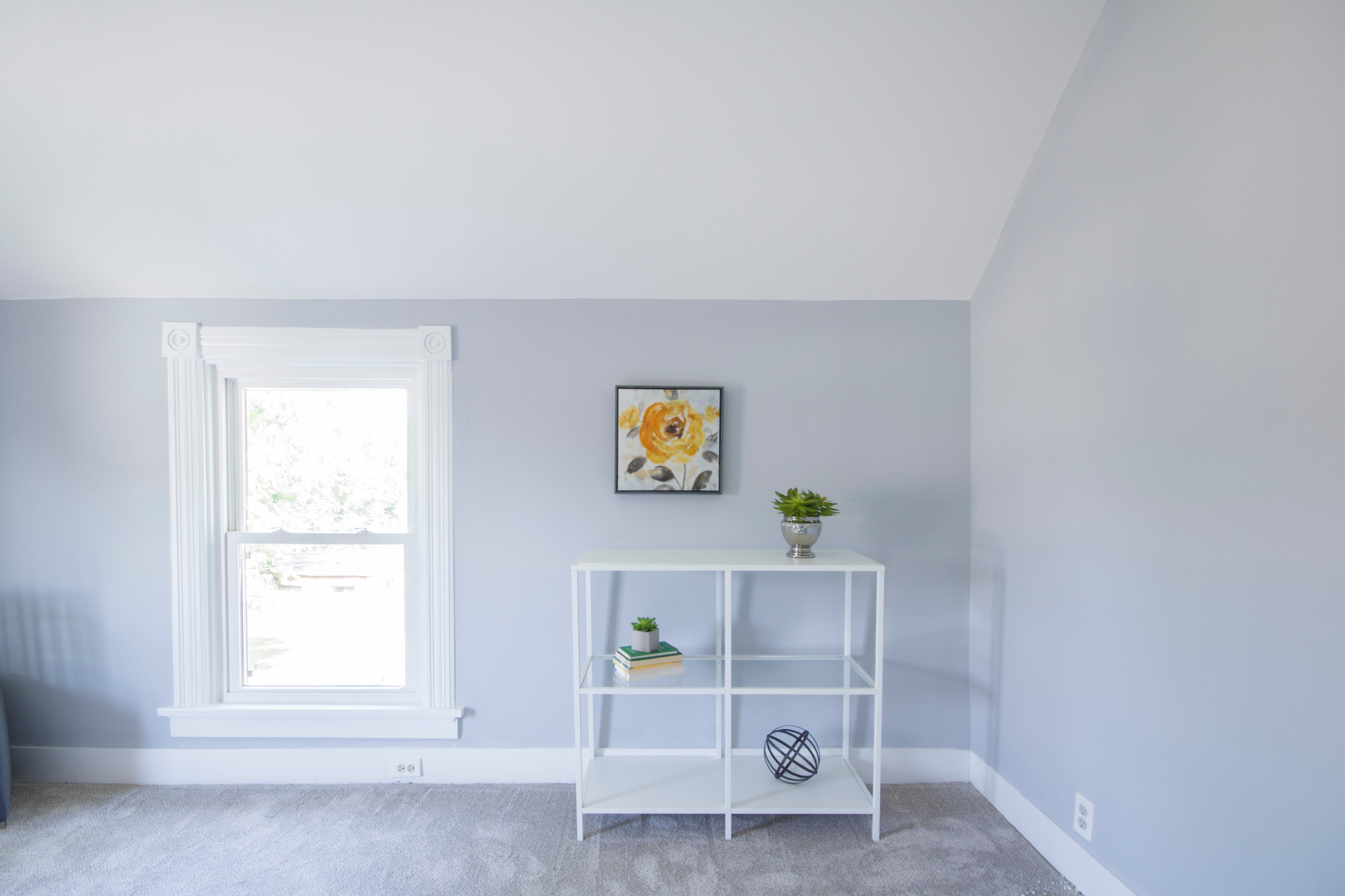 a minimalist white room with a simple shelf holding 3 succulents, a painting of a sunflower sits behind