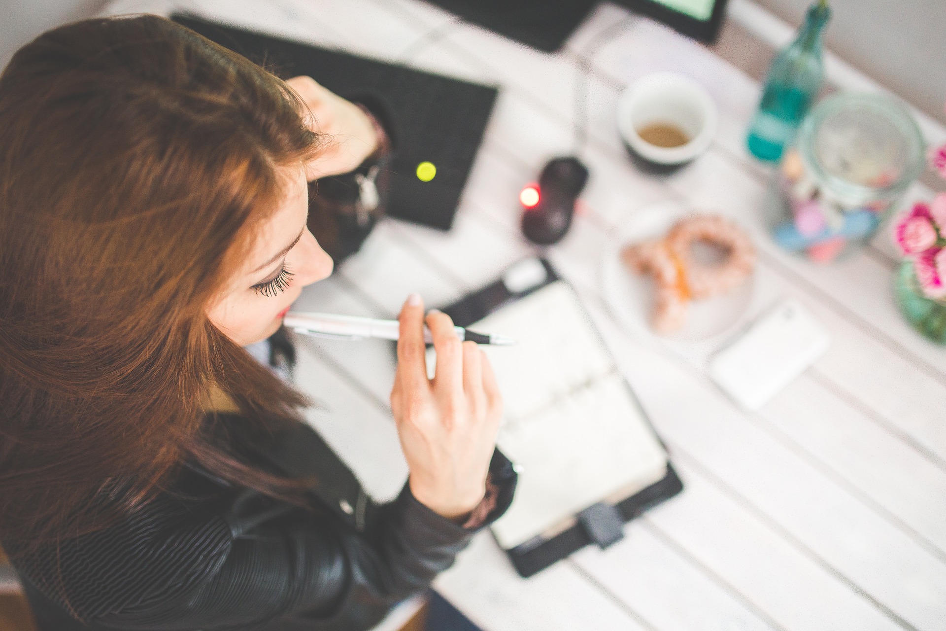 woman chewing on end of pen while looking at notebook on desk