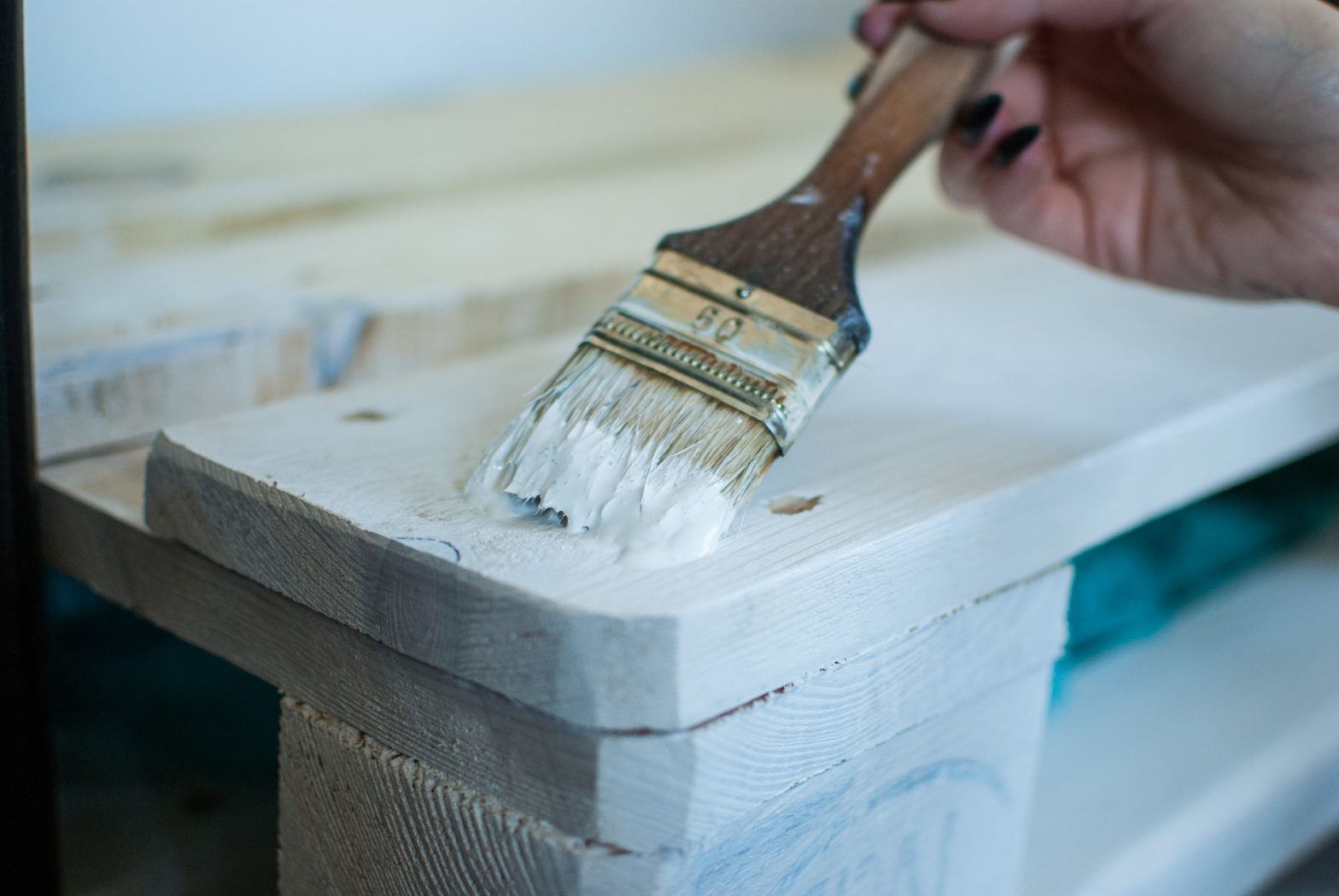 A person is holding a paintbrush and coloring the wood furniture with white color